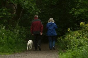 Retired couple walking their dog on a wooded trail.