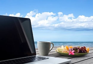 Laptop on a deck with cup of coffee and fruit.