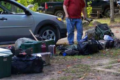 Man with a red shirt loading survival gear in to his car.
